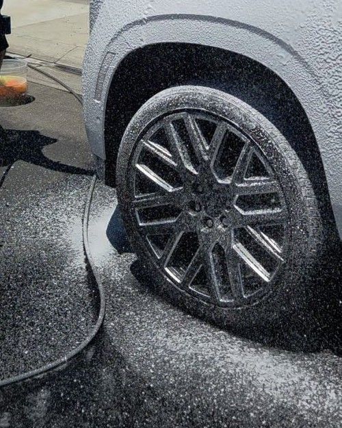 GMC Yukon Denali wheel under foam, mid-wash in the owner's driveway