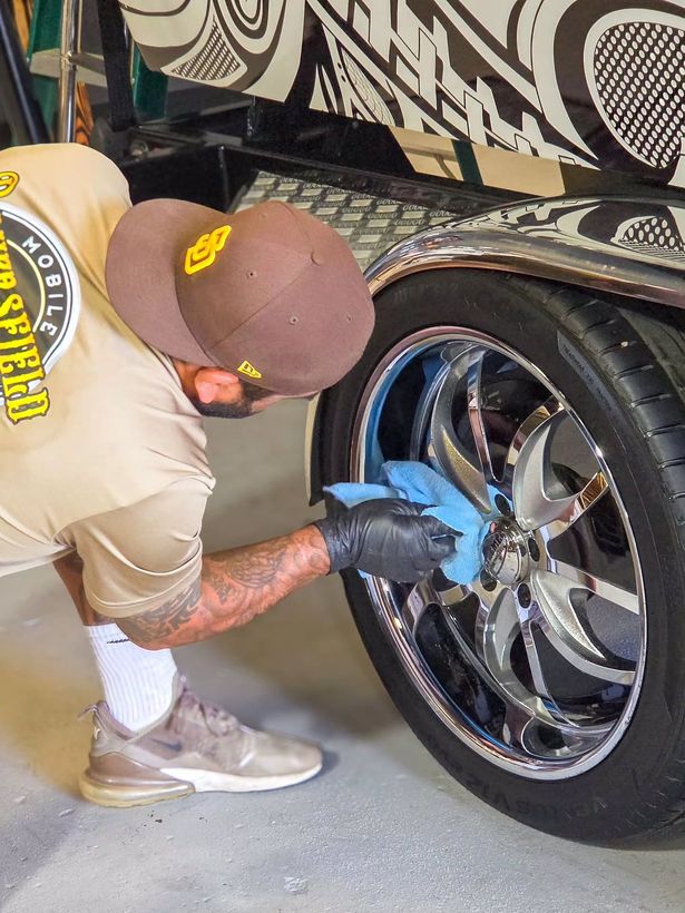 Detailer in a Bakersfield Finest shirt polishing a chrome trailer wheel